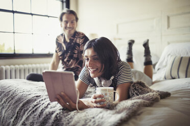 Lächelndes Paar, das sich auf dem Bett entspannt, Kaffee trinkt und ein digitales Tablet benutzt - CAIF04726