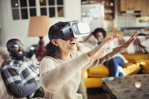 Frau gestikuliert und benutzt eine Virtual-Reality-Simulatorbrille im Wohnzimmer - CAIF04729