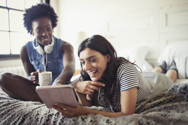 Lächelnde Frauen trinken Kaffee und benutzen ein digitales Tablet auf dem Bett - CAIF04732