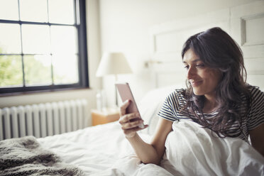 Junge Frau entspannt sich im Bett und schreibt eine SMS mit ihrem Smartphone - CAIF04737