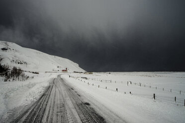 Road through snow covered landscape below stormy sky, Vik, Iceland - CAIF04746