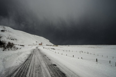 Straße durch schneebedeckte Landschaft unter stürmischem Himmel, Vik, Island - CAIF04746