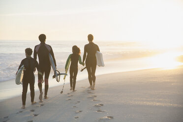 Familie in Neoprenanzügen spazieren mit Surfbrettern auf sonnigen Sommer Sonnenuntergang Strand - CAIF04771