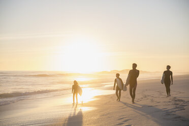 Silhouette family surfers walking with surfboards on idyllic, sunny summer sunset beach - CAIF04772