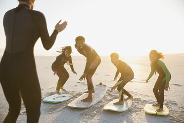 Surflehrer unterrichtet Familie auf Surfbrettern Surfen auf sonnigen Sommer Sonnenuntergang Strand - CAIF04780