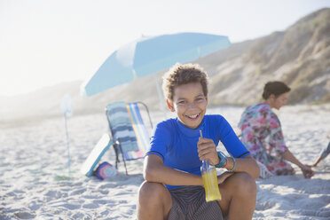 Porträt lächelnder, selbstbewusster Junge, der am sonnigen Sommerstrand Saft trinkt - CAIF04787