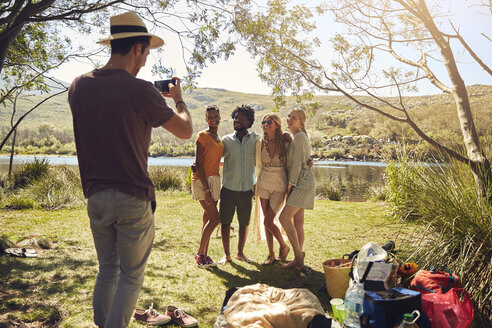 Junger Mann fotografiert Freunde am sonnigen Sommerufer - CAIF04800