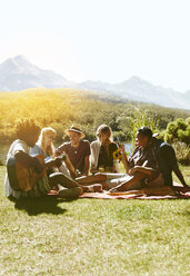 Junge Freunde hängen ab, spielen Gitarre und genießen ein Picknick im sonnigen Sommergras - CAIF04809