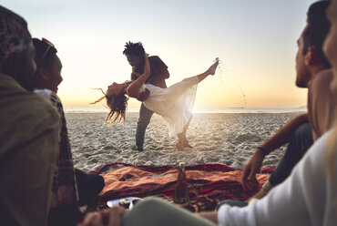 Verspieltes junges Paar tanzt am sonnigen Sommerstrand - CAIF04811
