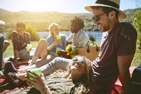 Junge Freunde entspannen sich bei einem Picknick am sonnigen Sommerufer - CAIF04815