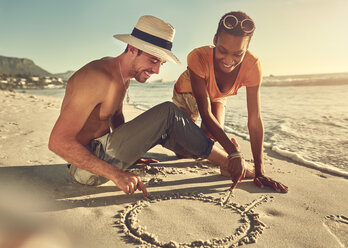 Junges Paar malt im Sand am sonnigen Sommerstrand - CAIF04816