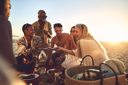 Lächelnde junge Freunde genießen ein Picknick am sonnigen Sommerstrand - CAIF04817