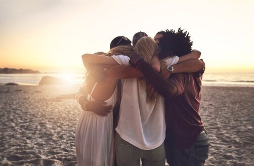 Junge Freunde umarmen sich bei Sonnenuntergang am Sommerstrand - CAIF04818