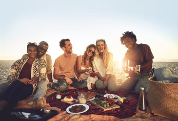 Portrait young friends hanging out, enjoying picnic on sunny summer beach - CAIF04819