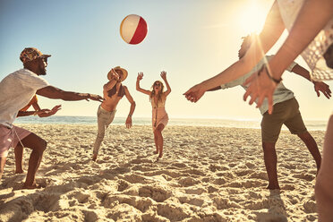 Verspielte junge Freunde spielen mit Strandball am sonnigen Sommerstrand - CAIF04822