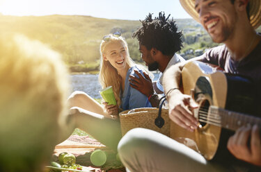 Junge Freunde spielen Gitarre und genießen ein sonniges Sommerpicknick - CAIF04824
