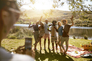 Junge Frau mit Fotohandy fotografiert Freunde beim sonnigen Sommerpicknick am Flussufer - CAIF04829