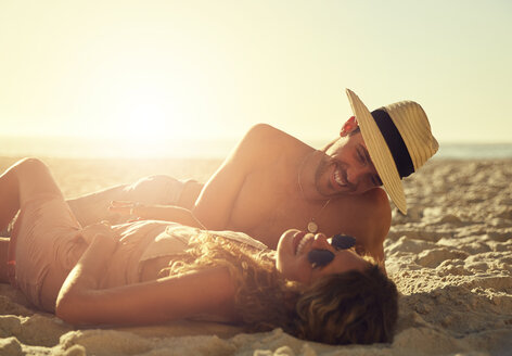 Lachendes junges Paar entspannt sich am sonnigen Sommerstrand - CAIF04830