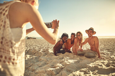 Junge Frau mit Fotohandy fotografiert Freunde am sonnigen Sommerstrand - CAIF04833