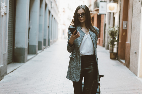 Junge Geschäftsfrau in der Stadt, die ihr Mobiltelefon überprüft, lizenzfreies Stockfoto