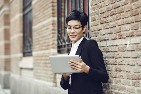 Portrait of content young businesswoman using tablet outdoors stock photo