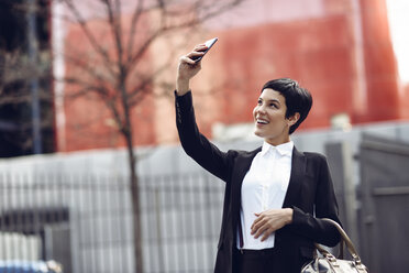 Porträt einer lächelnden jungen Geschäftsfrau, die ein Selfie mit ihrem Mobiltelefon macht - JSMF00062