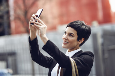 Porträt einer lächelnden jungen Geschäftsfrau, die ein Selfie mit ihrem Mobiltelefon macht - JSMF00063