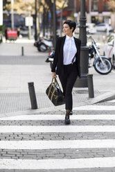 Lächelnde junge Geschäftsfrau beim Überqueren der Straße - JSMF00064