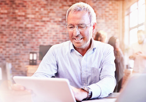 Lächelnder Geschäftsmann mit digitalem Tablet im Büro - CAIF04924