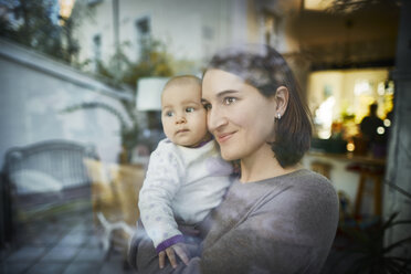 Smiling mother holding baby daughter at window - CAIF04926