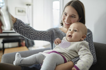 Lächelnde Mutter hält ihre kleine Tochter und macht ein Selfie mit der Handykamera - CAIF04931