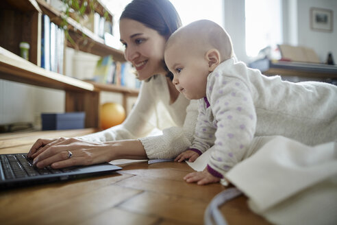 Kleine Tochter beobachtet Mutter beim Tippen auf dem Laptop auf dem Boden - CAIF04932