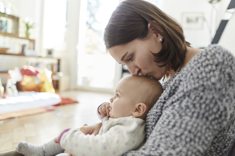 Mutter küsst ihre kleine Tochter auf den Kopf, lizenzfreies Stockfoto