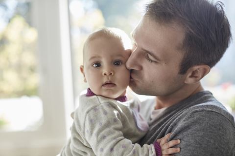 Porträt Baby Tochter wird von Vater auf die Wange geküsst, lizenzfreies Stockfoto