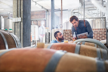 Male winemakers with digital tablet checking wood casks - CAIF04958