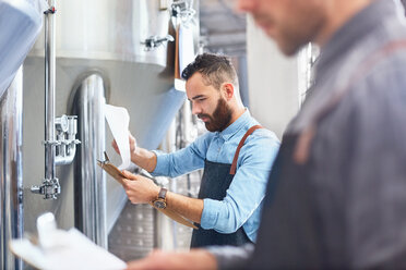 Male brewer with clipboard at vat in brewery - CAIF04965