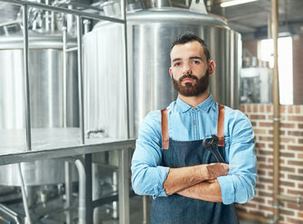 Porträt eines selbstbewussten männlichen Brauers vor einem Bottich in einer Brauerei - CAIF04980