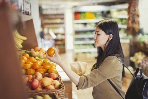 Junge Frau beim Einkaufen, Untersuchung von Orangen in einem Lebensmittelladen - CAIF04986