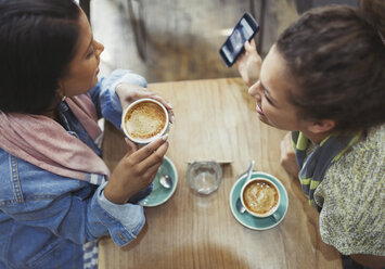 Freundinnen trinken Kaffee und benutzen ein Handy in einem Café - CAIF04988