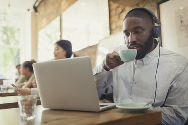 Mann mit Kopfhörern, der einen Laptop benutzt und Kaffee in einem Café trinkt - CAIF05002