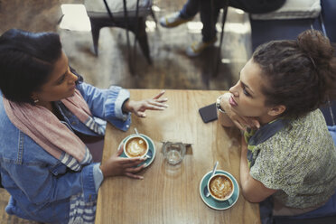 Junge Freundinnen unterhalten sich und trinken Cappuccino am Kaffeetisch - CAIF05010