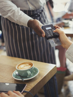 Ein Kunde bezahlt den Kellner mit einem Kreditkartenlesegerät am Kaffeetisch - CAIF05022