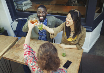 Begeisterte Freunde stoßen in einem Straßencafé mit frischen Saftgläsern an - CAIF05027