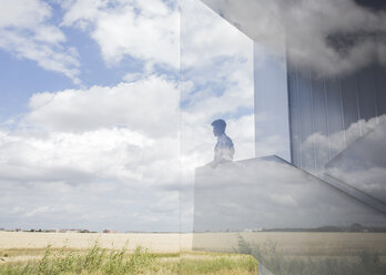 Nachdenklicher Geschäftsmann auf einem modernen Treppenabsatz, der aus dem Fenster auf den sonnigen blauen Himmel und die Wolken schaut - CAIF05031