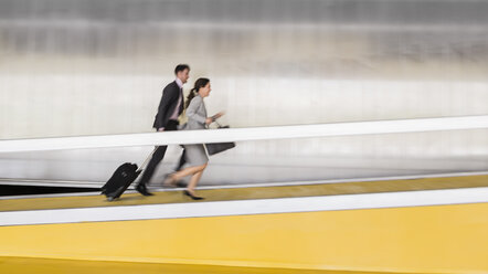 Geschäftsmann und Geschäftsfrau mit Koffer laufen die Flughafenrampe hinauf - CAIF05036
