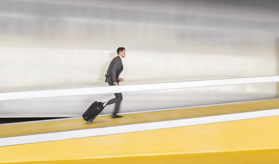Businessman running, pulling suitcase up airport ramp - CAIF05066