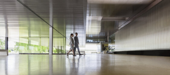 Businessman and businesswoman walking in modern office lobby - CAIF05075