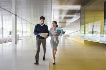 Geschäftsmann und Geschäftsfrau gehen und diskutieren Papierkram in einem modernen Bürokorridor - CAIF05076