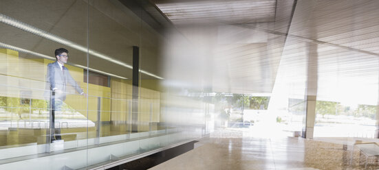 Pensive businessman standing at modern office window - CAIF05077