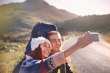 Junges Paar mit Rucksäcken wandern nehmen selfie mit Kamera-Handy auf sonnigen, abgelegenen Straße - CAIF05082